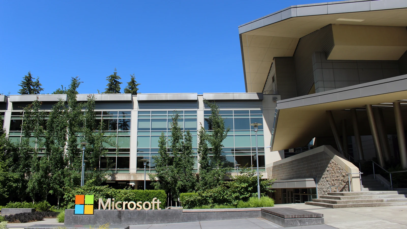A modern office or institutional building with large glass-paneled windows, gray metal cladding, broad overhanging roofs, columns, and a stepped entrance.